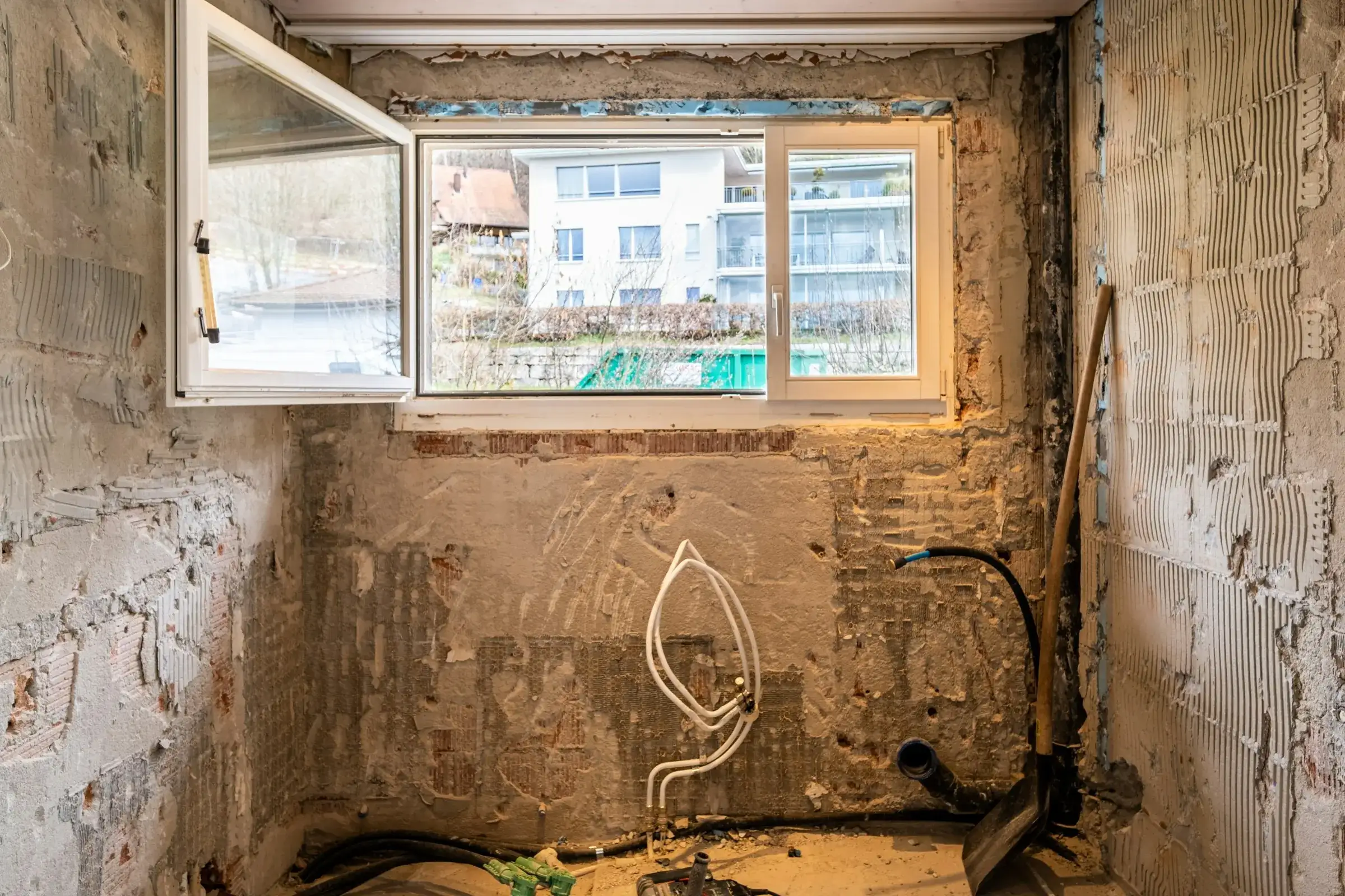 Before: bathroom stripped to rough brick and plaster, with loose water lines, an old window and debris on the floor.