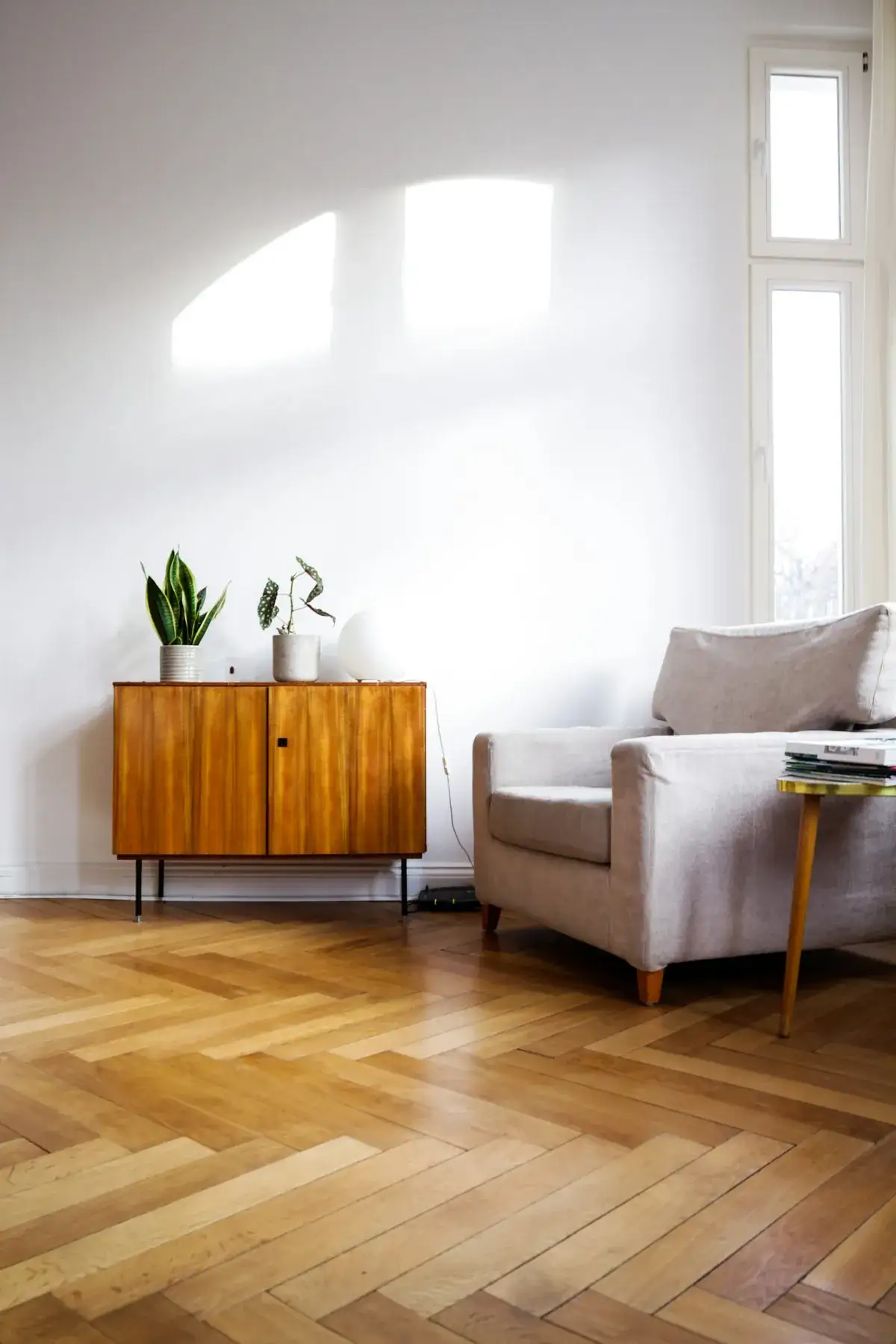 Sunny living room with a new oak herringbone floor, a mid-century teak sideboard and a pale armchair.