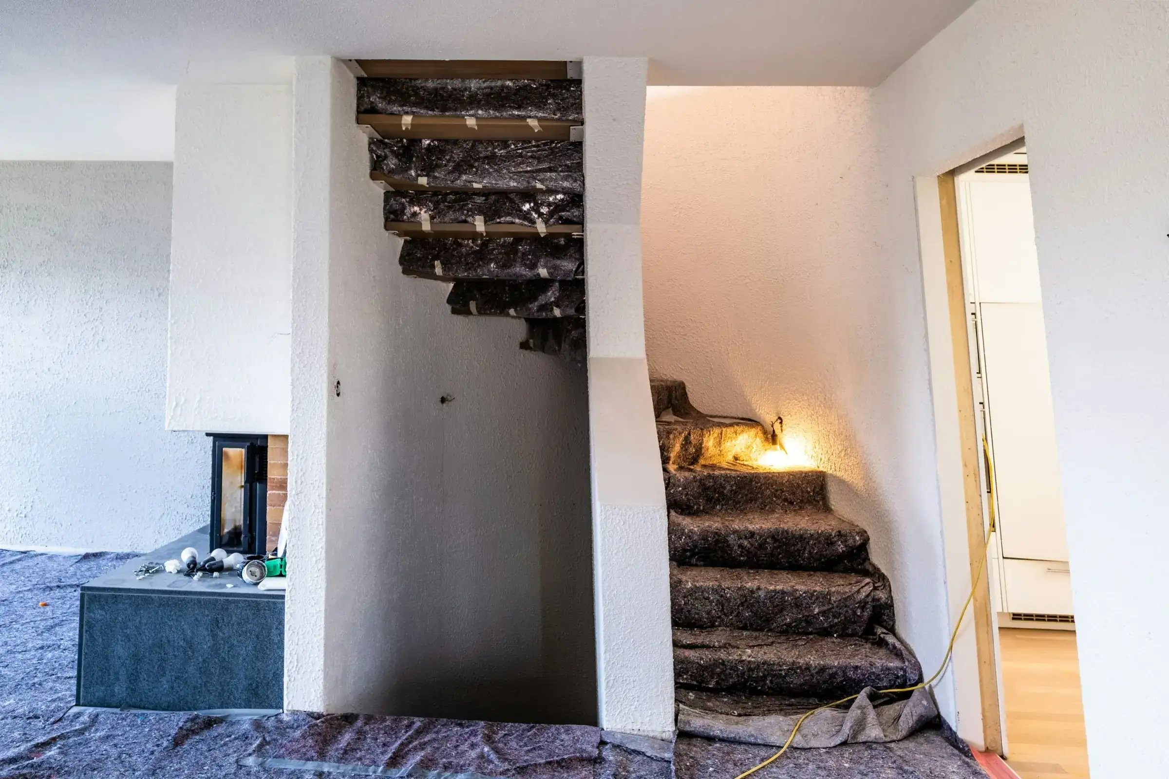 Before: main floor under renovation with protective sheets over the floor and old stair treads, and a work light on the steps.