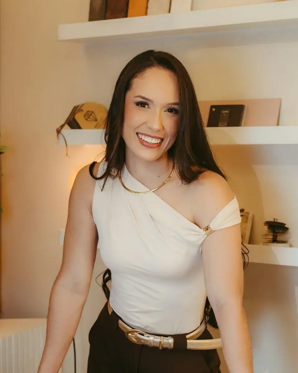 Sofia Marín, smiling at her desk in the design studio, with wood and stone samples on the shelves behind her.
