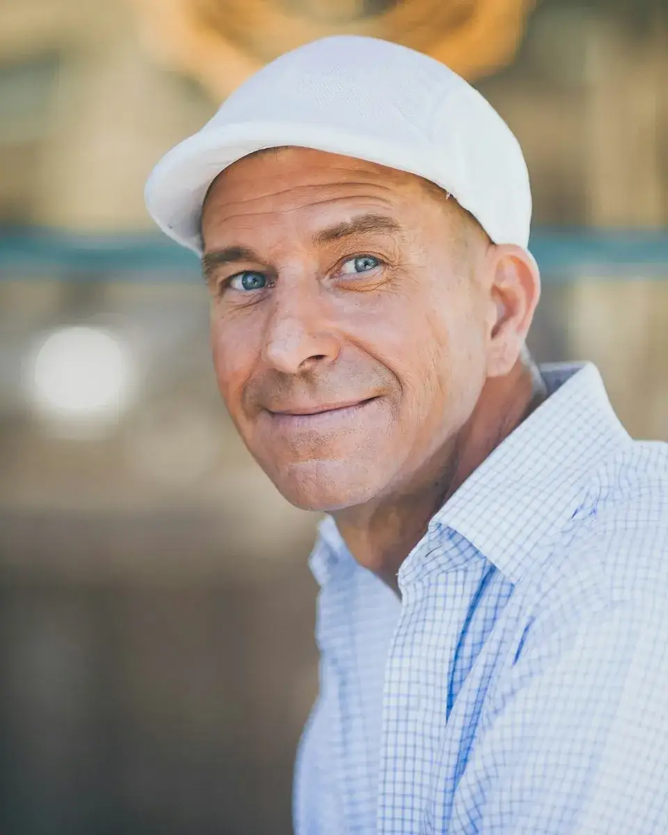 Mark Hollis in a white cap and a light blue shirt, smiling at the camera.
