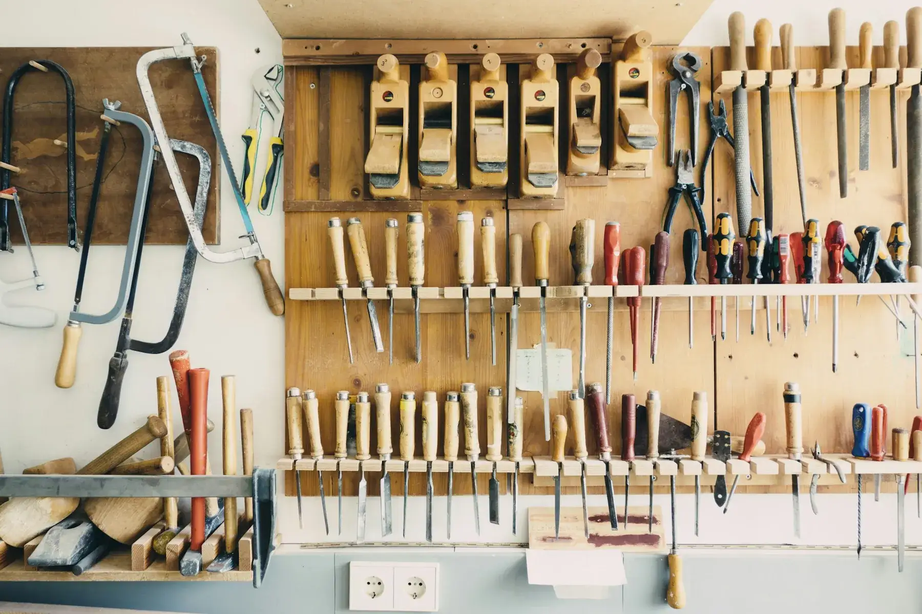 Hand tools hung neatly on a plywood wall in the workshop: saws, chisels, planes and screwdrivers.