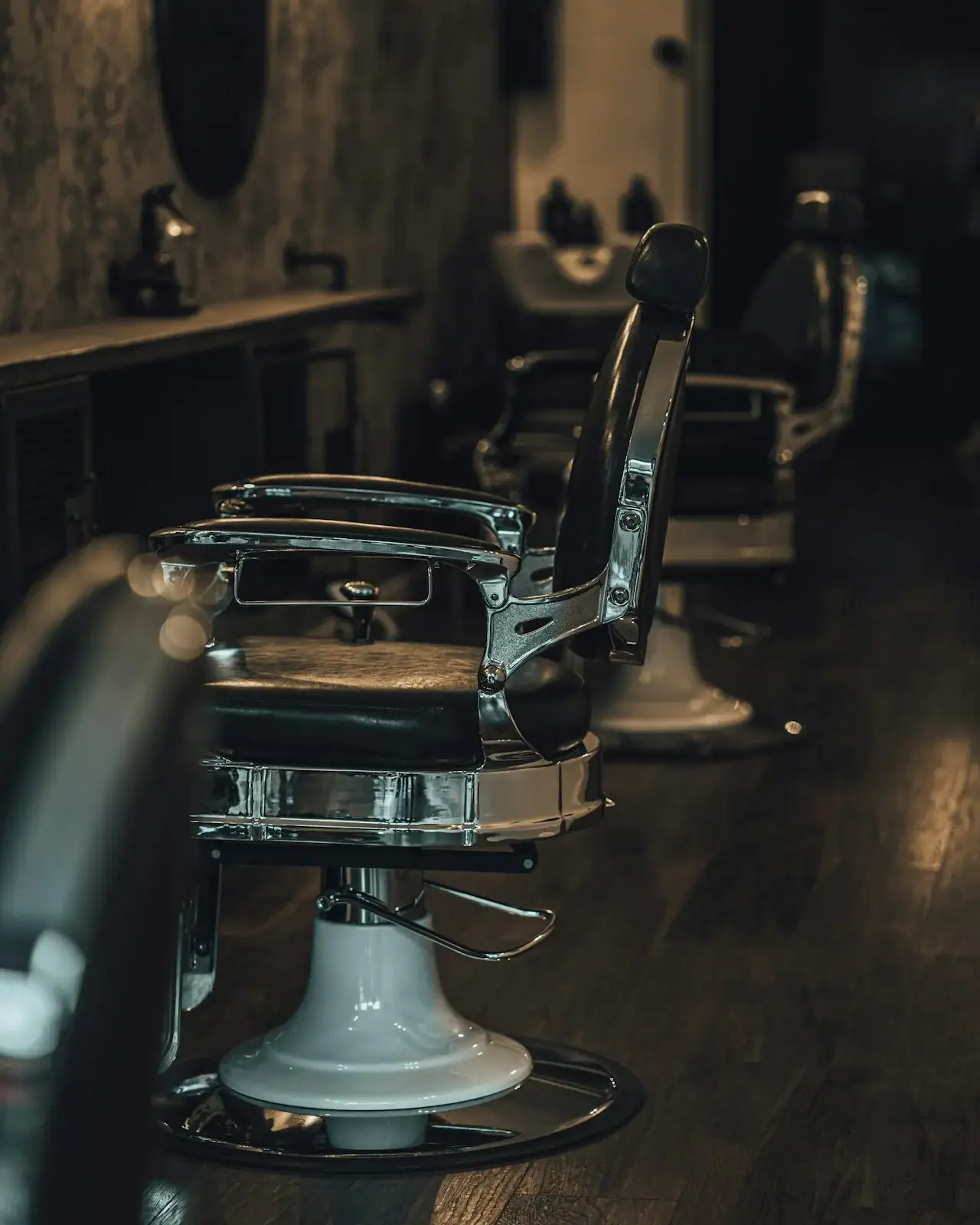 Chrome and black leather barber chairs in a dim, wood-floored shop.