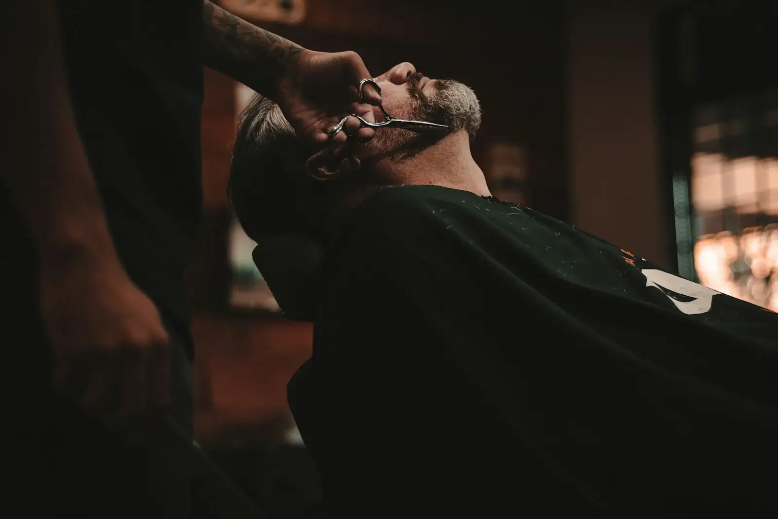 Client reclined in a barber chair while the barber finishes his beard.