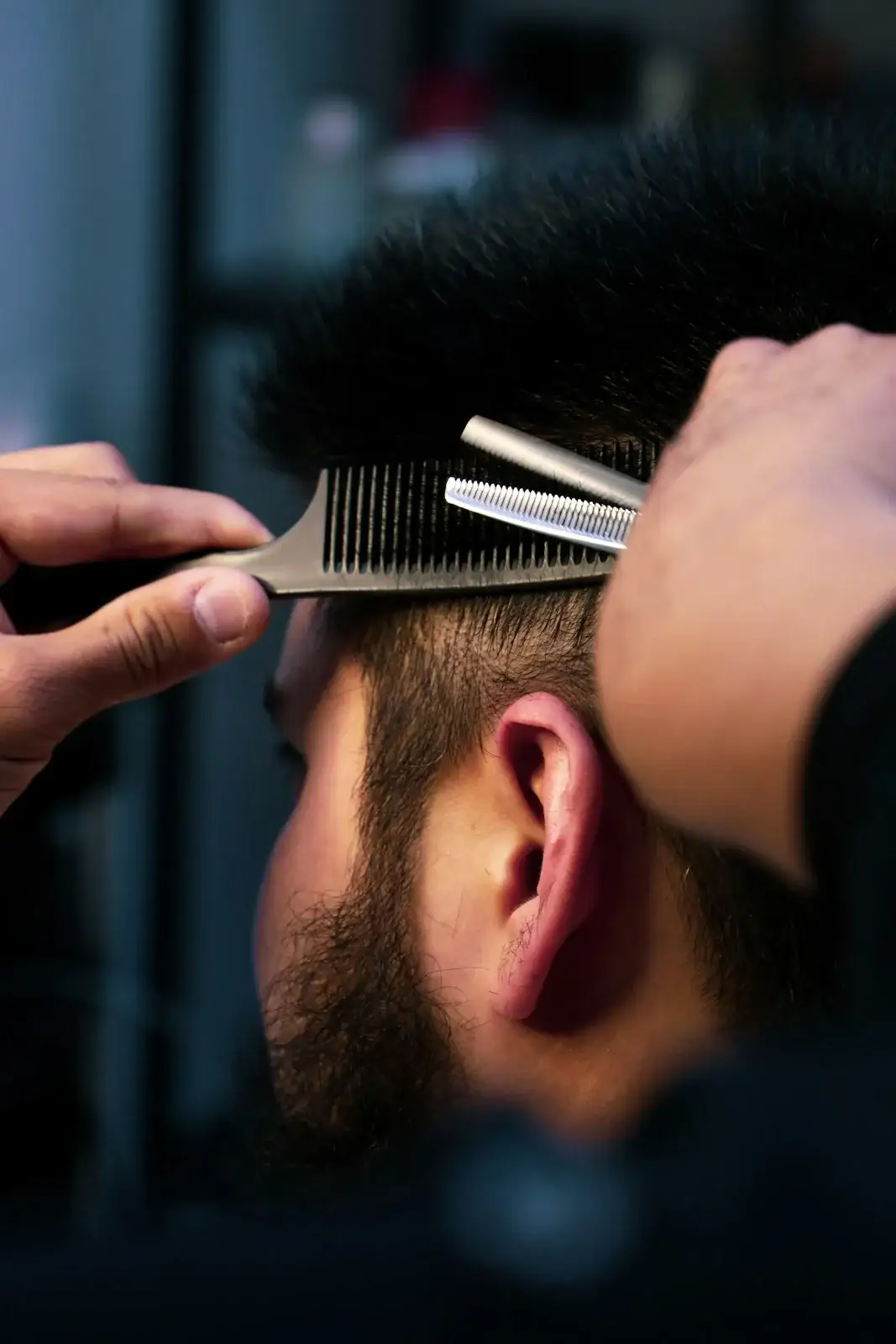 Close-up of thinning shears and a comb working through short dark hair.