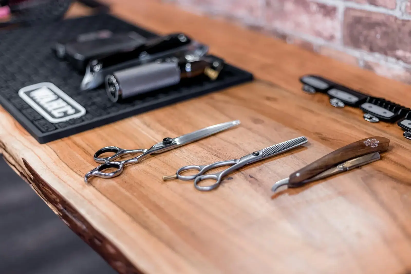 Scissors, a straight razor and clippers laid out on a live-edge wooden counter.